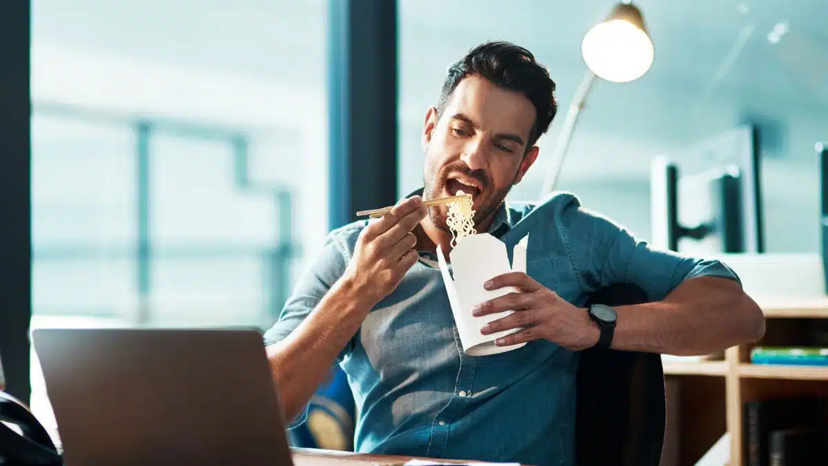 man eating while looking at laptop